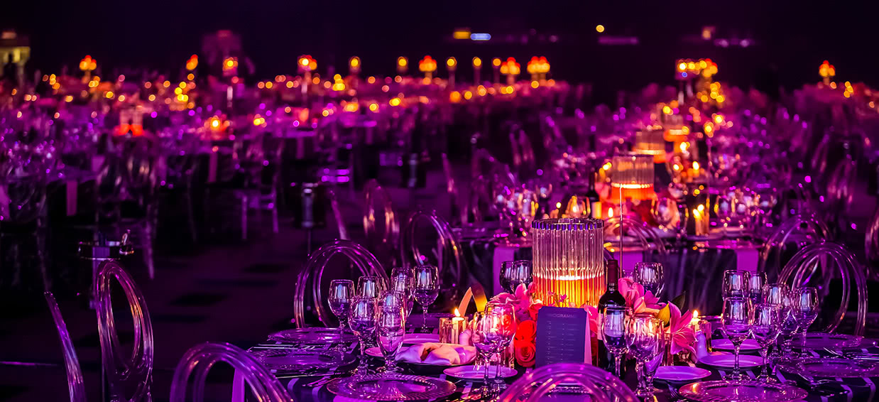 Event tables set for a celebration, lit in magenta and orange
